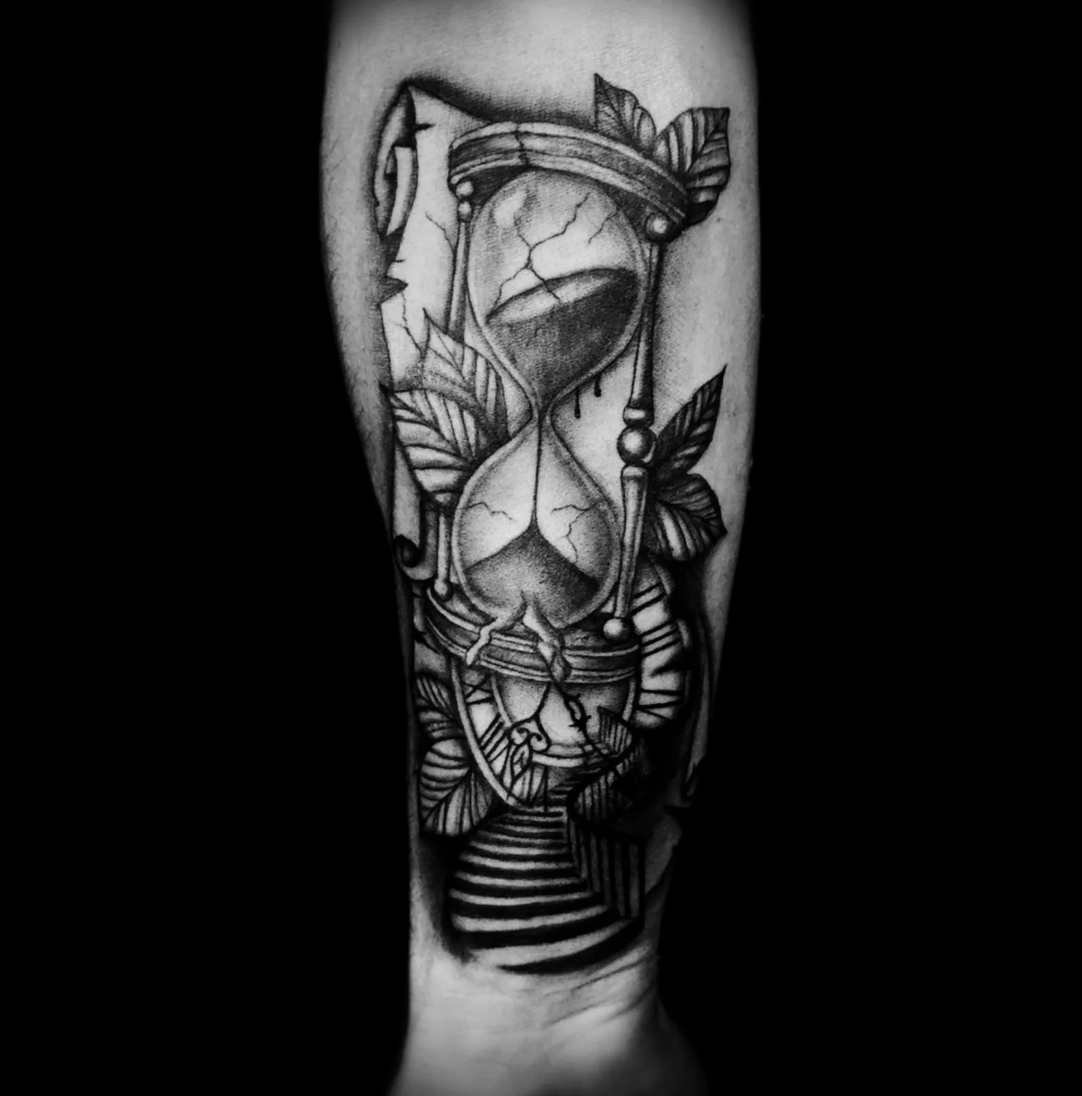 Graficzny tatuaż pękniętej klepsydry z liśćmi na przedramieniu, wykonany w PM Tattoo w Legnicy
