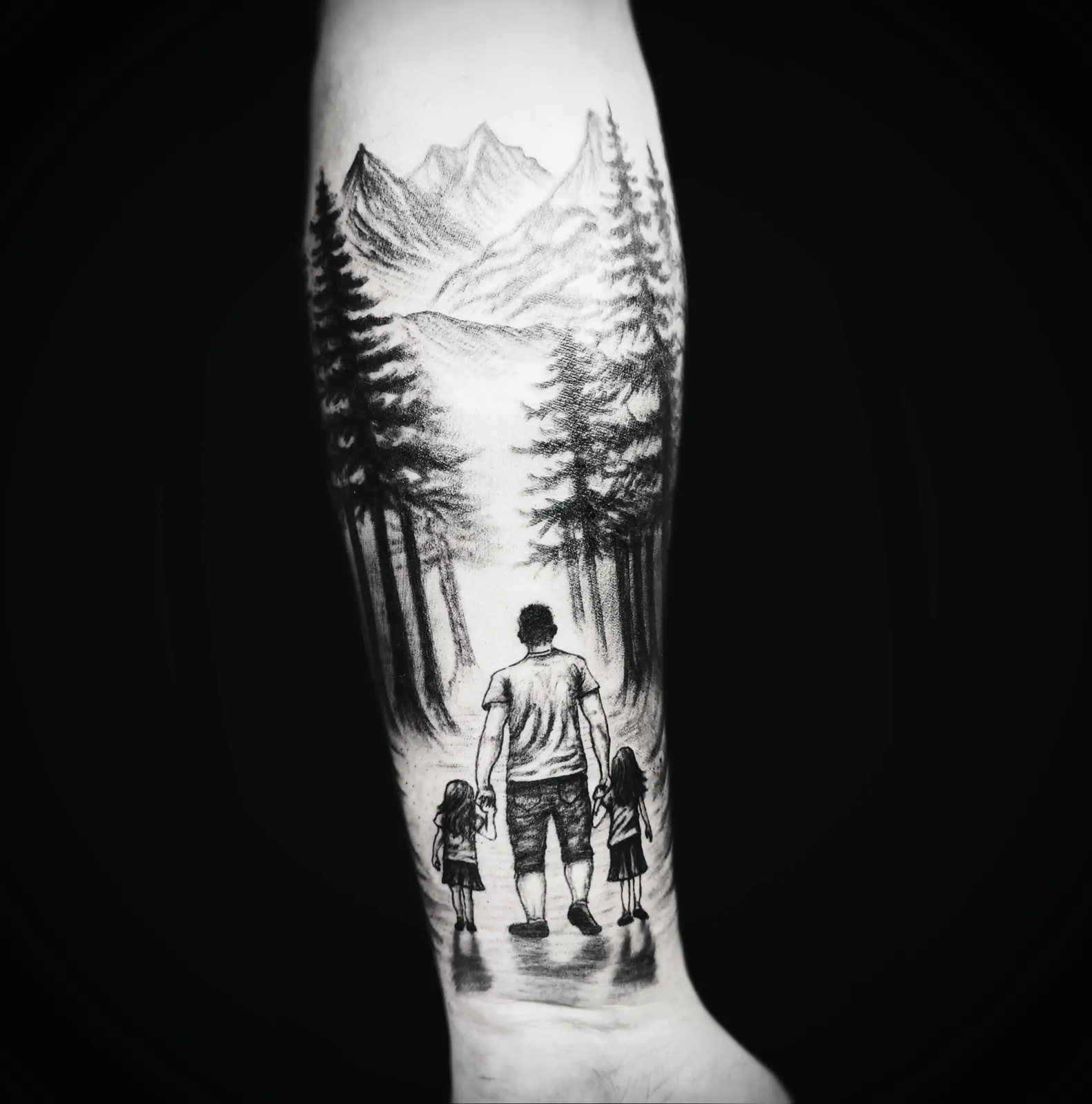 Graficzny tatuaż górskiego lasu z sylwetkami ojca i dzieci na przedramieniu, wykonany w PM Tattoo w Legnicy
