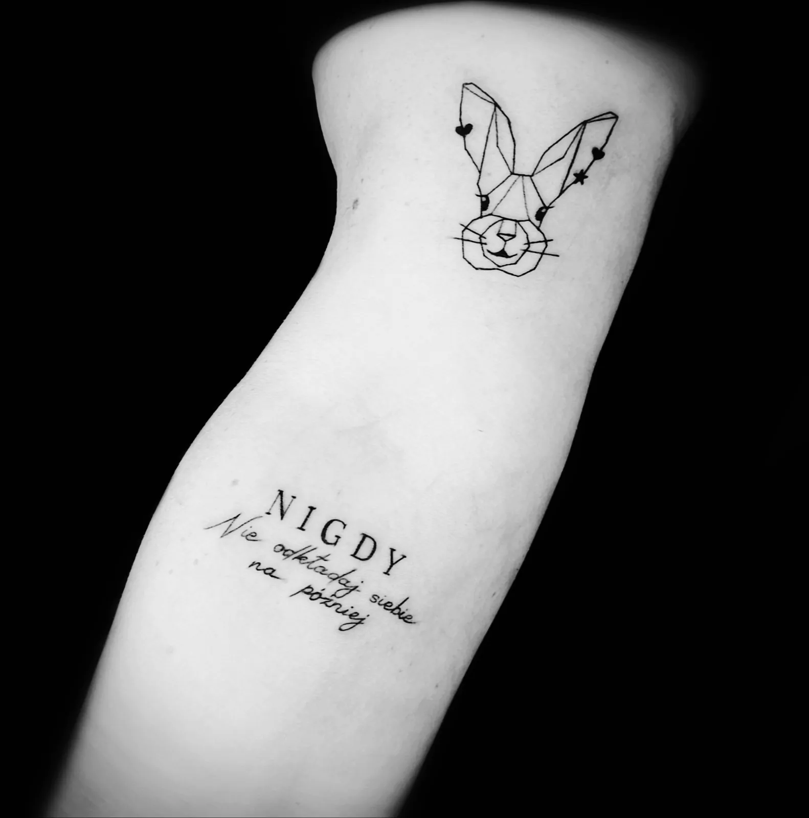 Minimalistyczny geometryczny tatuaż królika z napisem na ramieniu, wykonany w PM Tattoo w Legnicy