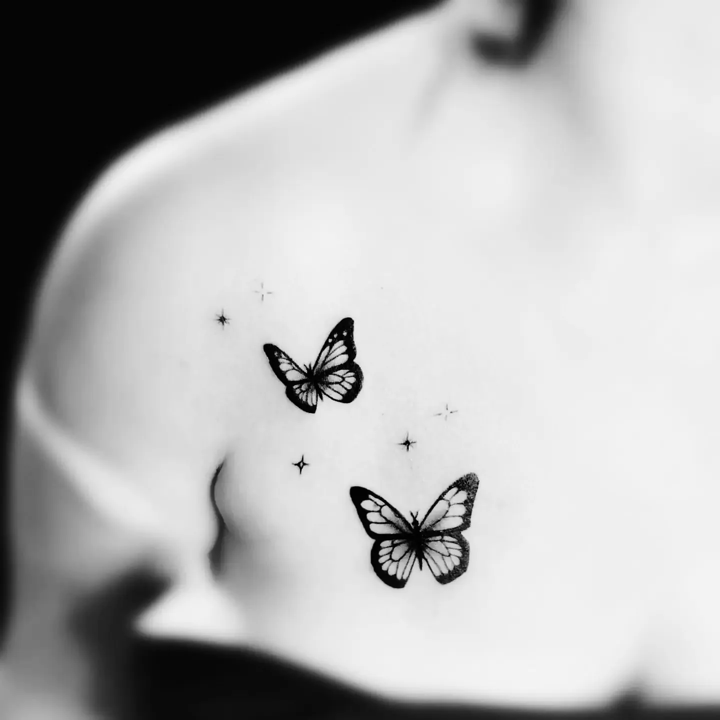 Delikatny tatuaż dwóch motyli z gwiazdkami na obojczyku, wykonany w PM Tattoo w Legnicy