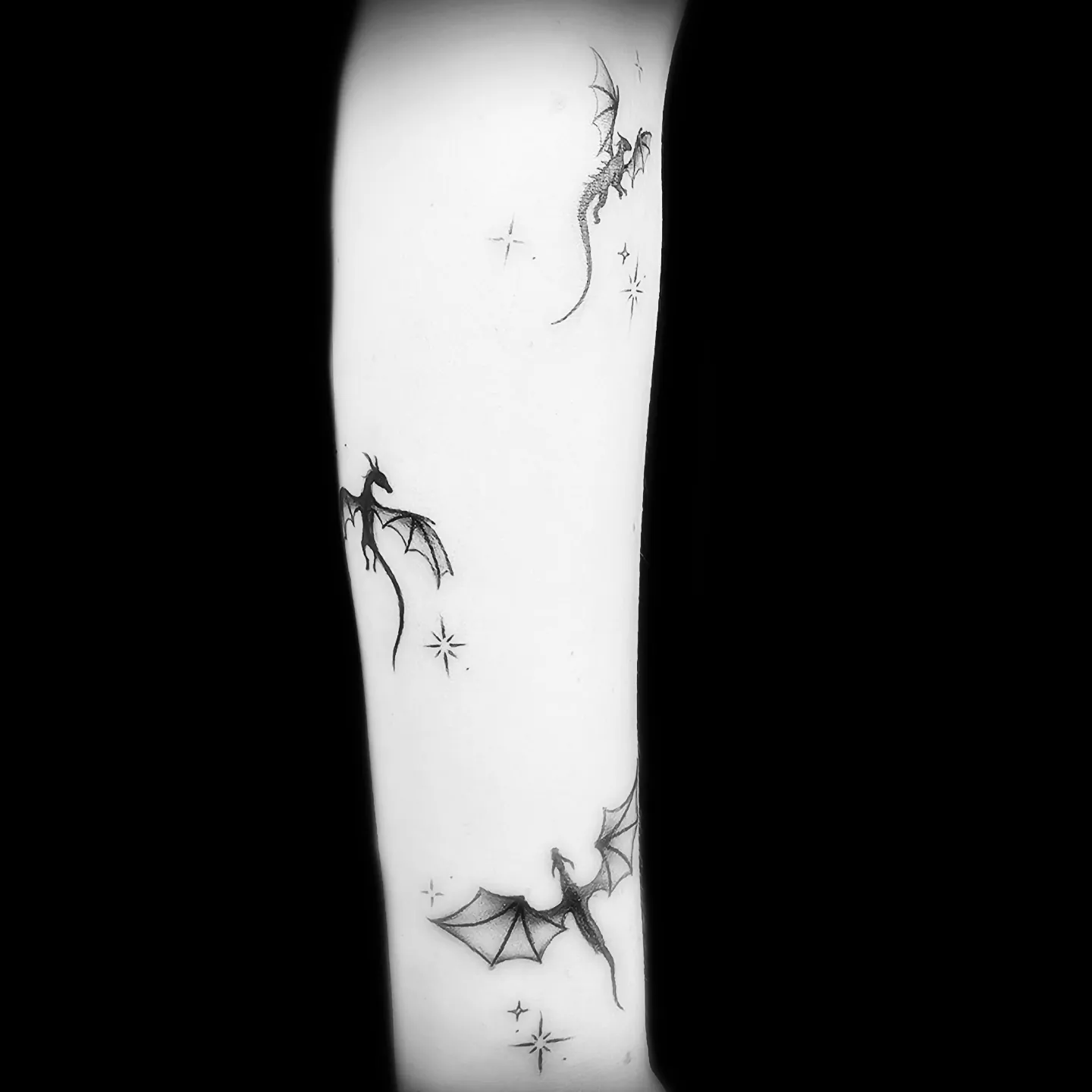Tatuaż fine line małych smoków z gwiazdkami na ramieniu, wykonany w PM Tattoo w Legnicy